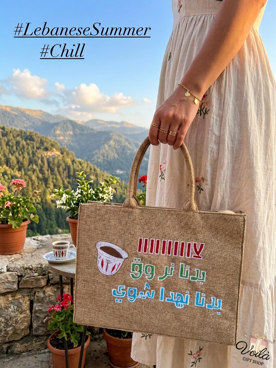 Woman holding a burlap tote bag with Arabic text and Lebanese coffee cup illustration in front of a mountain view.