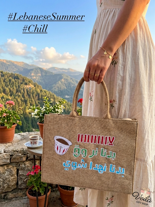 Woman holding a burlap tote bag with Arabic text and Lebanese coffee cup illustration in front of a mountain view.