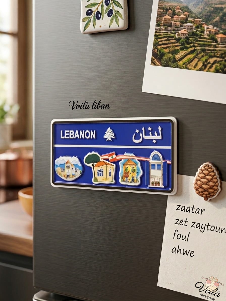 Blue decorative Lebanese license plate fridge magnet featuring illustrations of traditional village houses with red tile roofs, iconic triple-arched windows, and the Lebanese flag, placed on a refrigerator next to a handwritten shopping list.