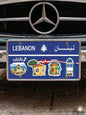 Blue decorative Lebanese license plate mounted on a classic car, featuring illustrations of traditional village houses with red tile roofs, iconic triple-arched windows, the Lebanese flag, and Arabic text reading Bil Qaleb.