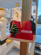 Red earrings with a green tree design and 'Lebanon' text on a stand.