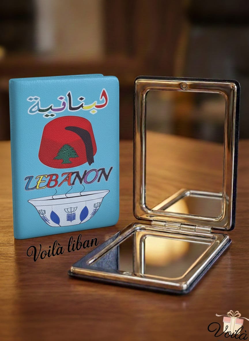 Compact mirror and blue notebook with Lebanese design on a wooden surface