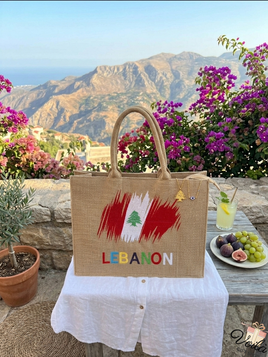Handcrafted jute tote bag featuring the Lebanese flag and colorful Lebanon text set against a scenic mountain backdrop
