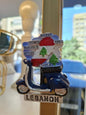 Fridge magnet shaped like a scooter with Lebanese flag design and text on a blurred background