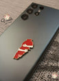 Red and white map-shaped pin on a dark phone case with 'Voila Gift Shop' branding.