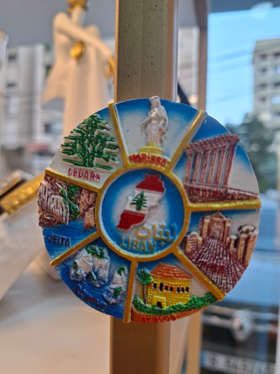 Colorful round magnet with Lebanese landmarks and text on a stand.