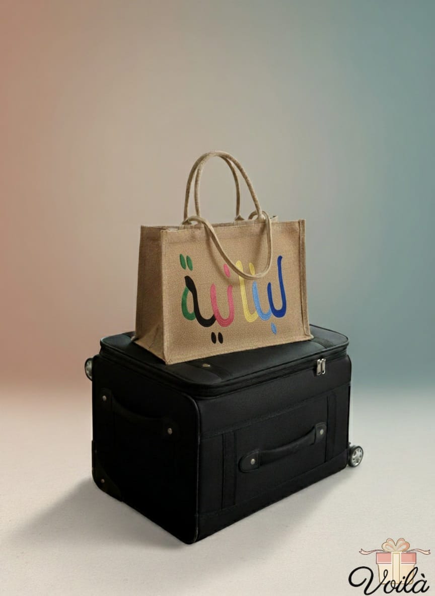 Brown tote bag with colorful text on a black suitcase against a gradient background