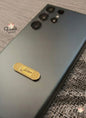 Smartphone with a gold badge on a textured surface, branded 'Voila'.