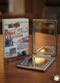 Compact mirror with a travel guidebook on a wooden surface