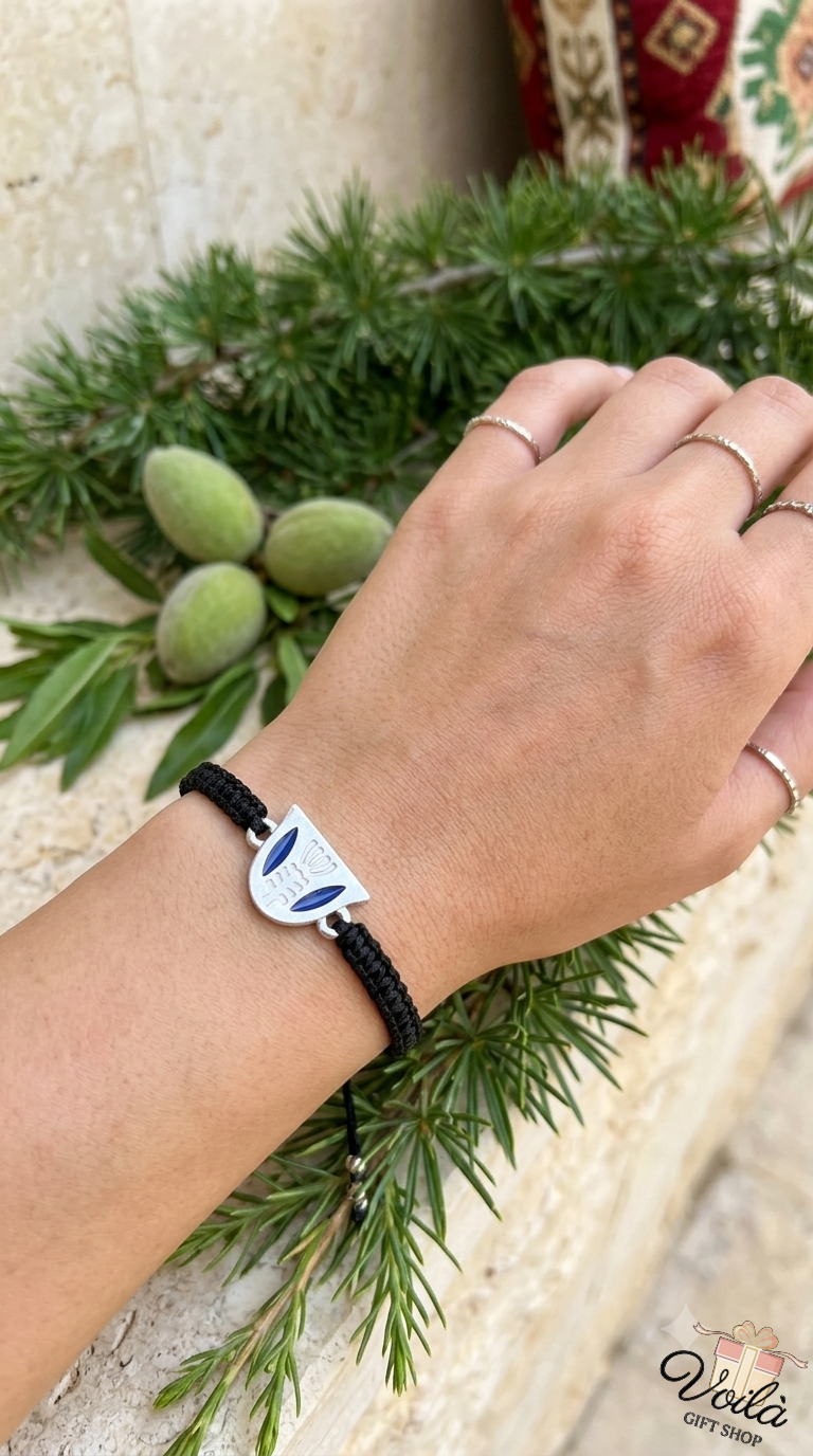 Handcrafted Phoenician ship silver cord bracelet worn on a wrist with green almonds and cedar branches in the background.