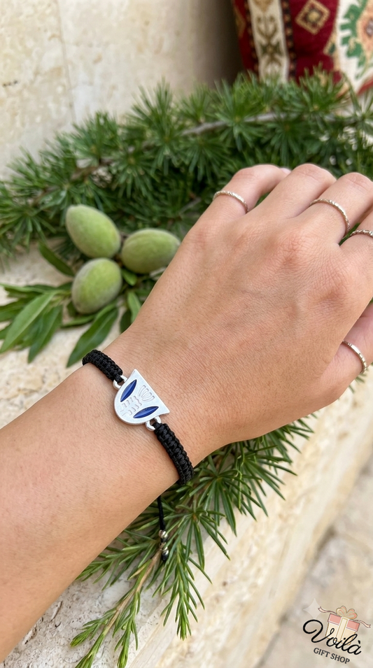 Handcrafted Phoenician ship silver cord bracelet worn on a wrist with green almonds and cedar branches in the background.