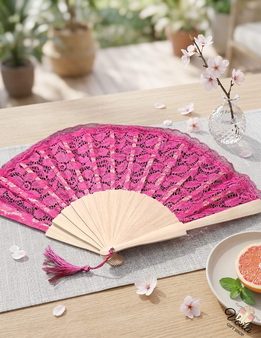 Elegant pink lace folding fan with wooden handle and tassel on a table with cherry blossoms