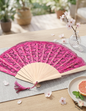 Elegant pink lace folding fan with wooden handle and tassel on a table with cherry blossoms