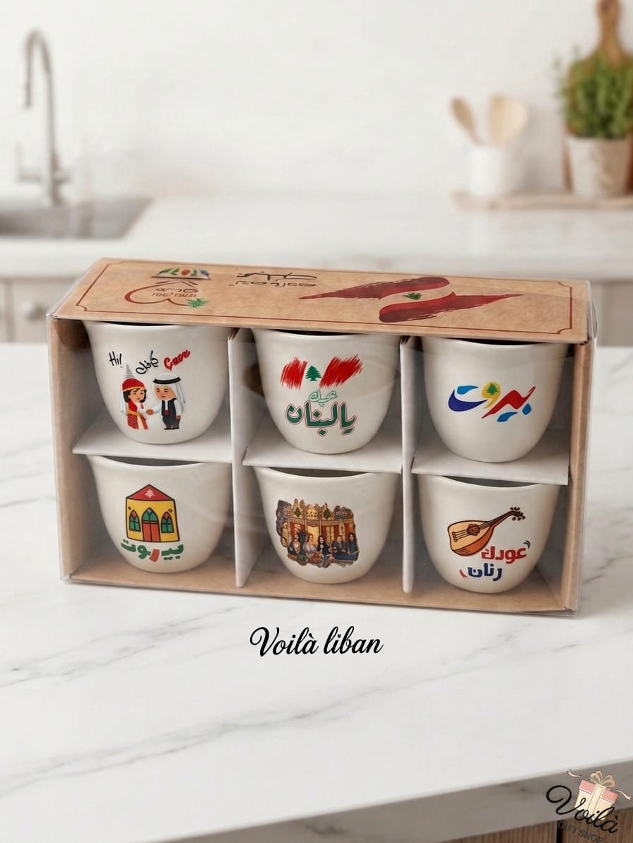 Set of six premium white ceramic Arabic coffee cups featuring iconic Lebanese nostalgic motifs including traditional dress, an oud, and heritage architecture, presented in a kraft display box on a white marble countertop.