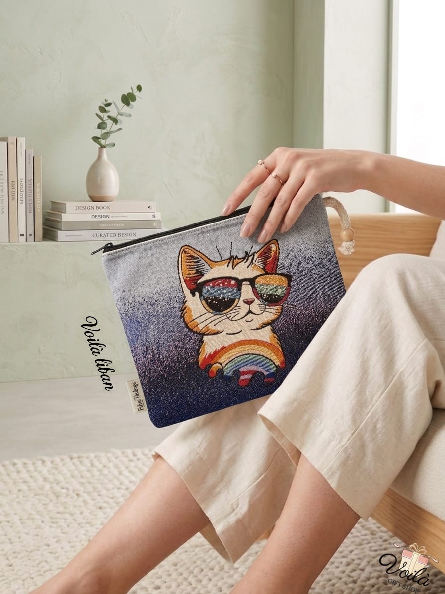 Woman sitting in a bright room holding a premium woven tapestry pouch featuring a playful cat wearing colorful sunglasses sitting above a vibrant rainbow.