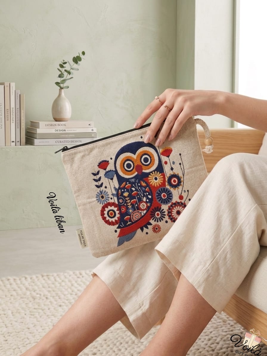 Woman sitting in a bright room holding a premium woven tapestry pouch featuring a colorful folk-art owl and intricate floral design on a cream background.