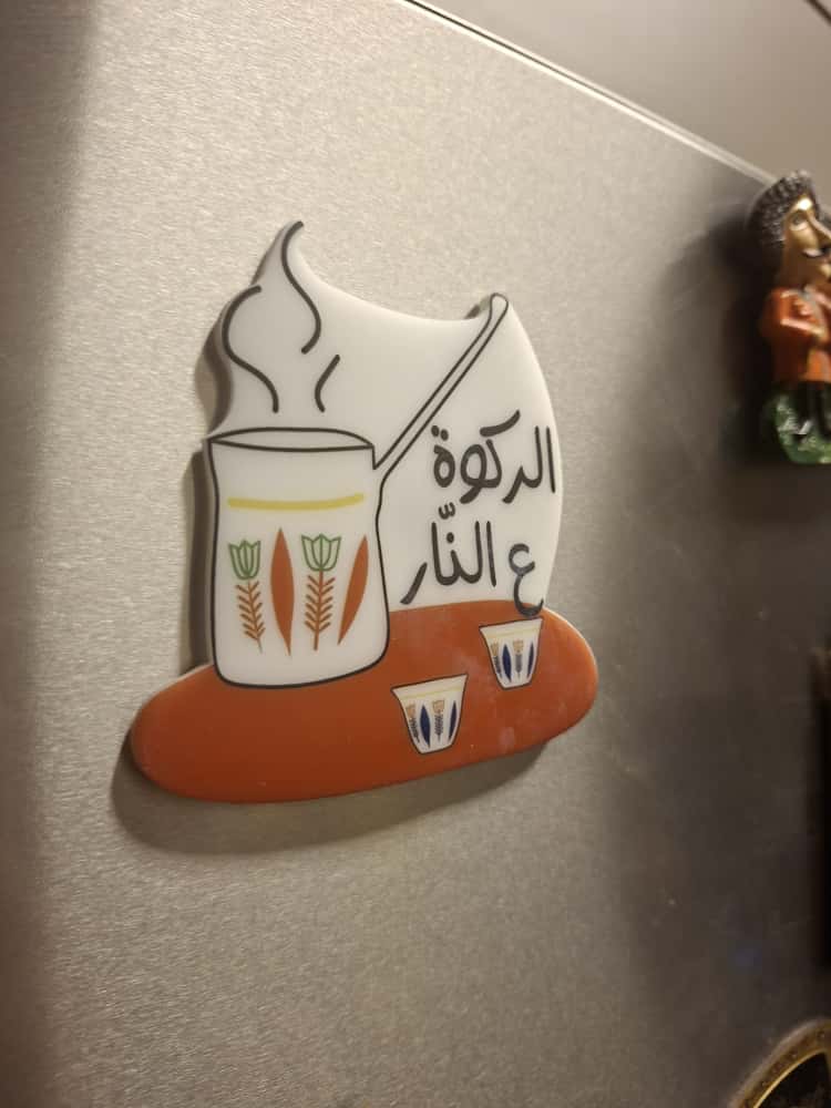 Decorative magnet with a design of a candle and Arabic text on a metallic surface.