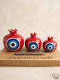 Set of three premium vibrant red ceramic pomegranate vases in cascading sizes, featuring a striking traditional blue concentric circle motif, displayed elegantly on a wooden board.