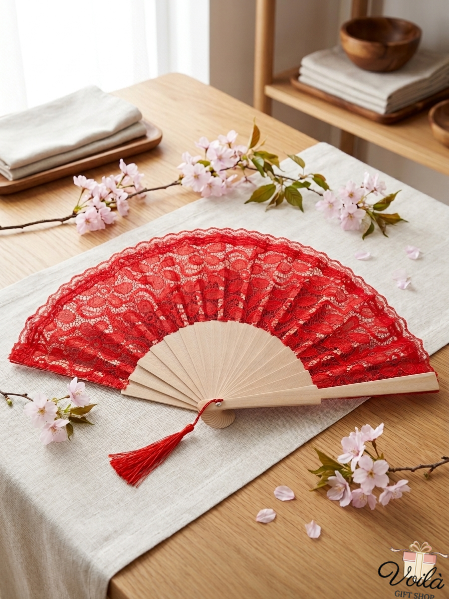 Elegant red lace folding hand fan with a wooden frame and red tassel, displayed on a table with cherry blossoms.