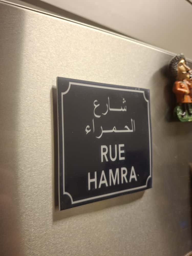Street sign for 'Rue Hamra' with Arabic text on a wall.