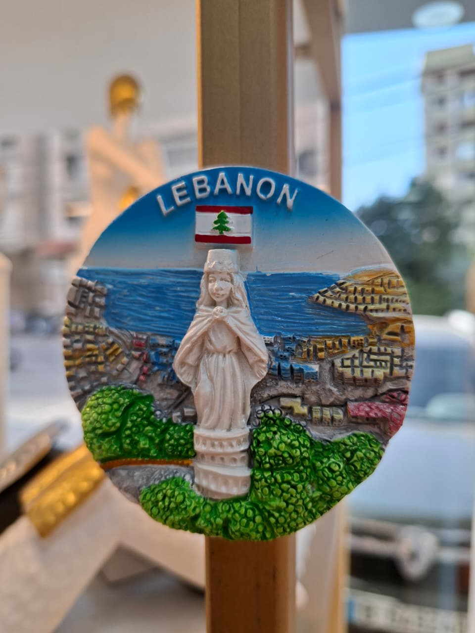 Decorative magnet with a scenic view of Lebanon featuring a statue and flag.