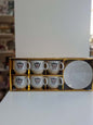 Set of six white coffee cups with a logo in a gold box on a white surface.