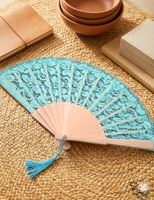 Elegant turquoise lace hand fan with natural wooden ribs and a matching tassel on a woven mat