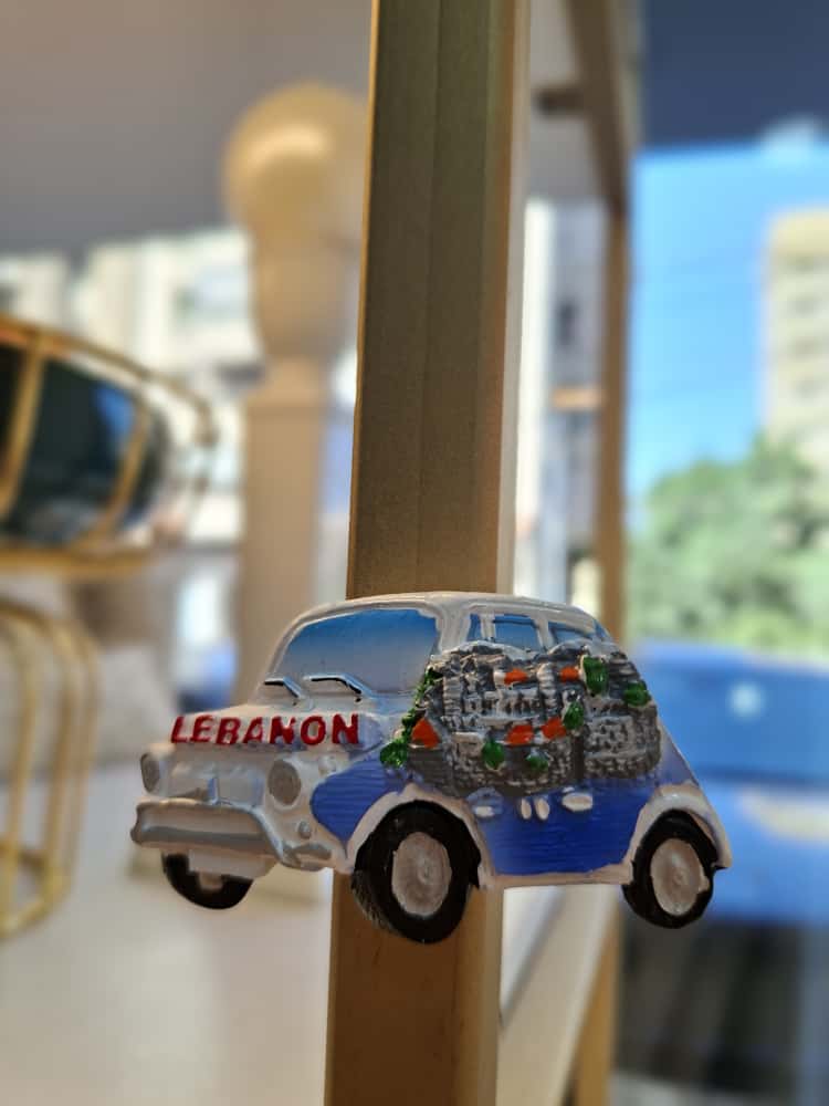 Fridge magnet of a blue and white van with 'Lebanon' text on a wooden stand.