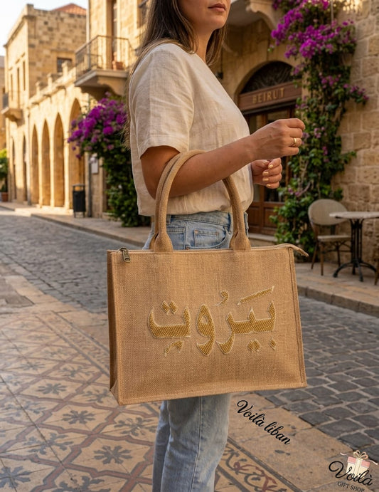Elegant woman carrying a natural jute tote bag with gold crystal Beirut Arabic calligraphy on a classic city street.