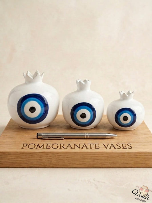 Set of three premium white ceramic pomegranate vases in cascading sizes, featuring a striking traditional blue concentric circle motif, displayed elegantly on a wooden board.