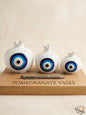 Set of three premium white ceramic pomegranate vases in cascading sizes, featuring a striking traditional blue concentric circle motif, displayed elegantly on a wooden board.
