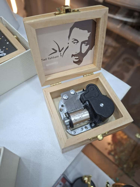Wooden music box with mechanical components and a portrait inside, on a reflective surface.